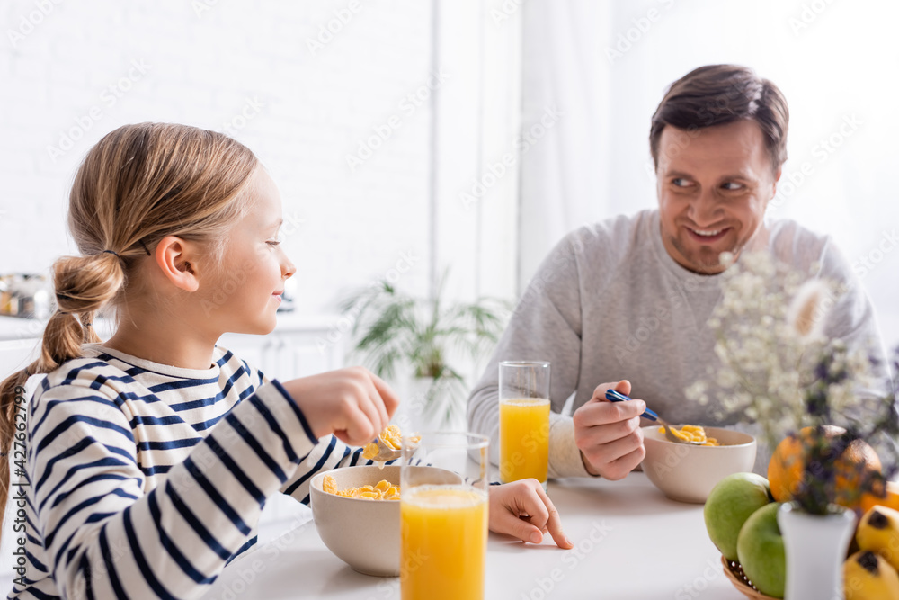 smiling father looking at daughter while eating corn flakes for breakfast smiling father looking at daughter while eating corn flakes for breakfast