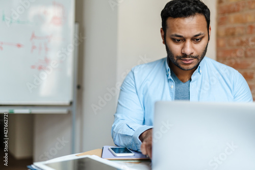 Middle eastern unshaven man working with laptop while sitting at desk