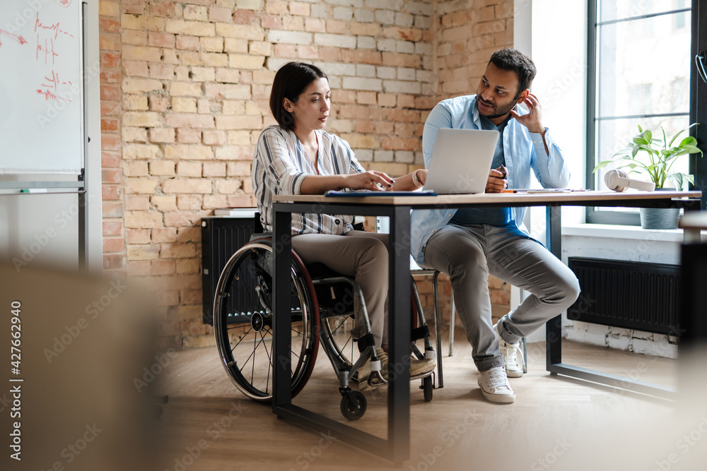 © Drobot Dean - Multiracial young two colleagues smiling while working with laptop