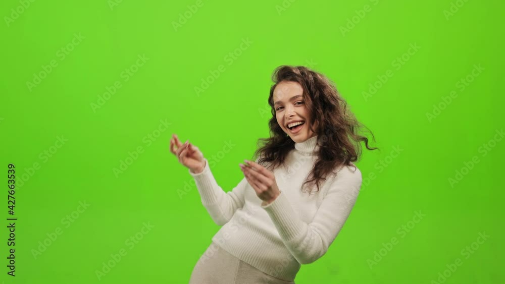 The woman is standing and looking at the camera. She is snapping her fingers and dancing. She is smiling. She is standing on a green background. Green screen. 4K