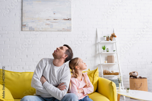 offended man with daughter sitting with crossed arms and sticking out tongues photo