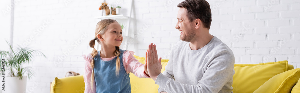 cheerful father and daughter giving high five while smiling at each other, banner cheerful father and daughter giving high five while smiling at each other, banner