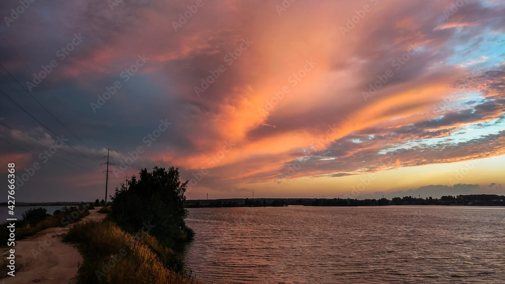 Sunset over the lake with beautiful clouds illuminated by the rays of the setting sun