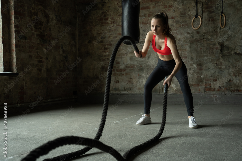 Woman with battle ropes exercise in the fitness gym. sportswoman working out with at gym