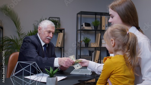 Mother and daughter child kid come to bank office to get a loan for open own business, buy housing. Real estate. Banker man reviews income statement and agrees to provide a loan and giving dollar cash