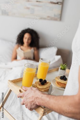 partial view of man holding tray with tasty breakfast near happy african american girlfriend on blurred background