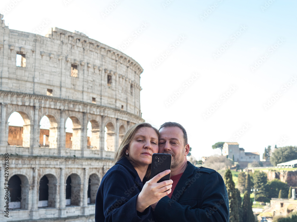 Couple of young people is taking a selfie near the Colosseum in Rome, Italy