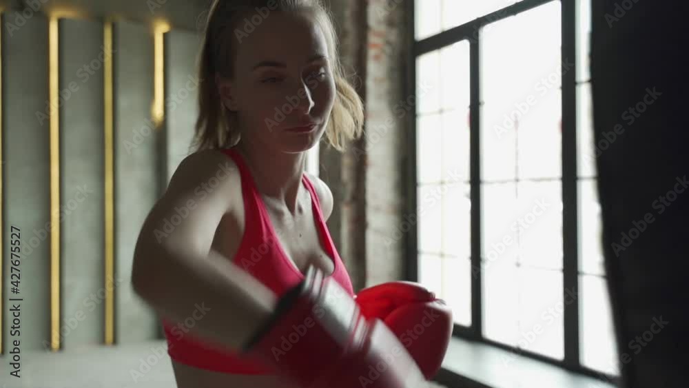 Woman in boxing gloves beats a punch bag. Woman in sportswear, exercising at the gym.