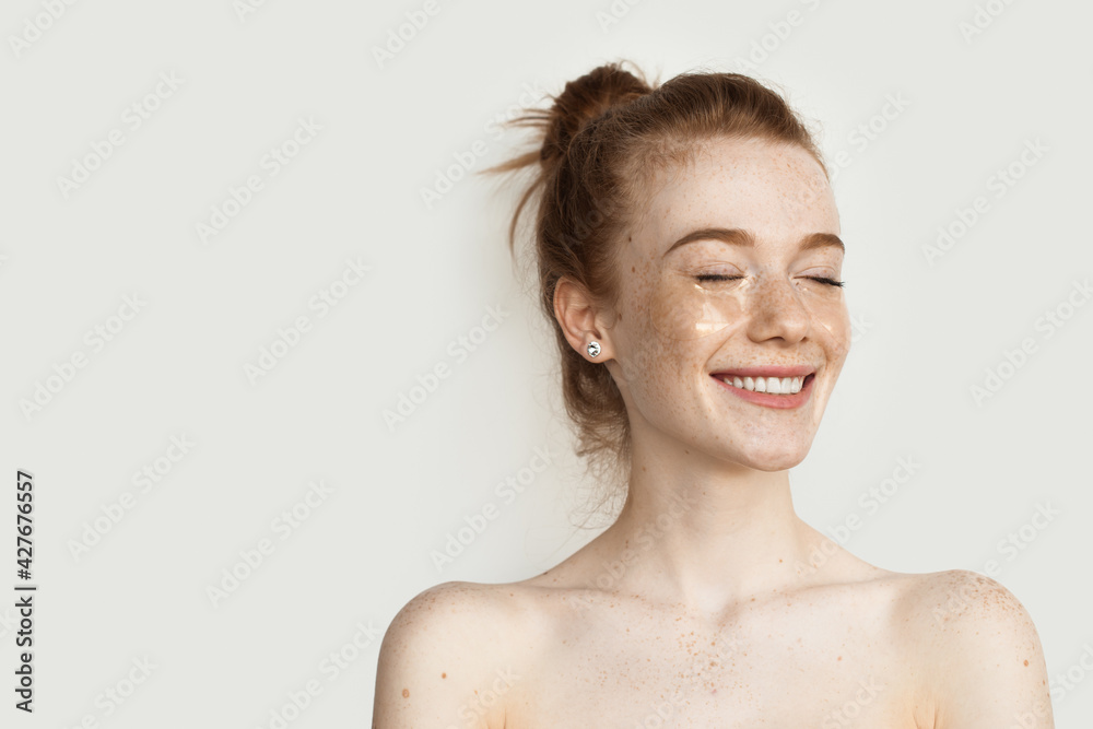 Ginger woman with eye patches is smiling on a studio wall with bare shoulders Ginger woman with eye patches is smiling on a studio wall with bare shoulders