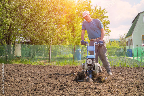 A man cultivates the soil in the garden using a motor cultivator - tiller photo