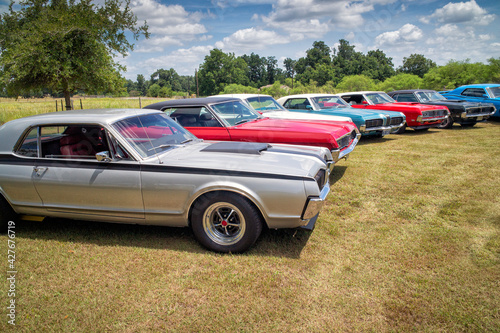 Vintage classic muscle cars parked together in field for club cruise or show