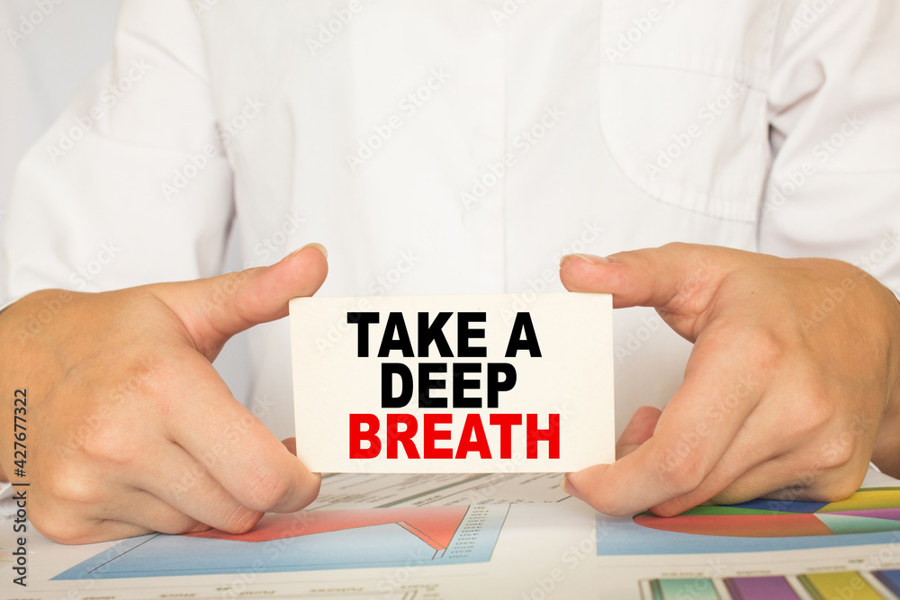 a man in the office holds a card with text TAKE A DEEP BREATH . business concept a man in the office holds a card with text TAKE A DEEP BREATH . business concept