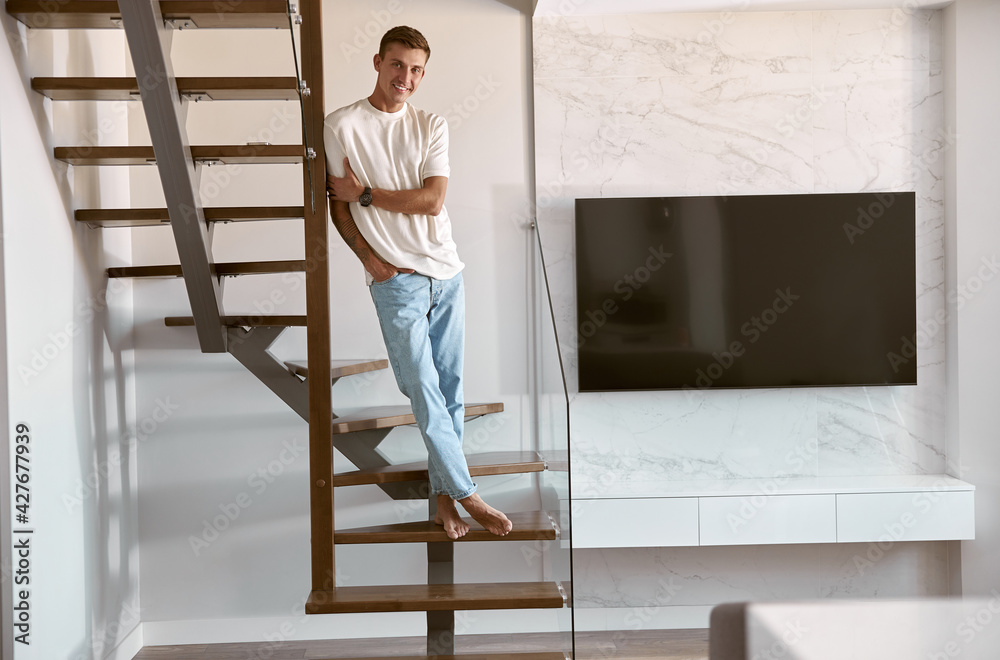 Relaxing happy caucasian man on the minimalistic stairs in modern light apartment