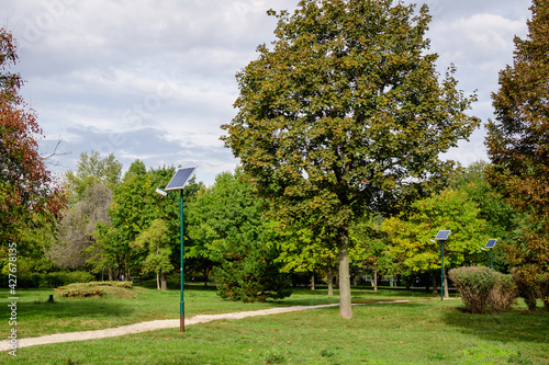 Long alley and a lighting pole activated with an attached blue solar panel in Parcul Izvor (Izvor Park) in Bucharest, Romania, with cloudy sky in the background, in a summer day.