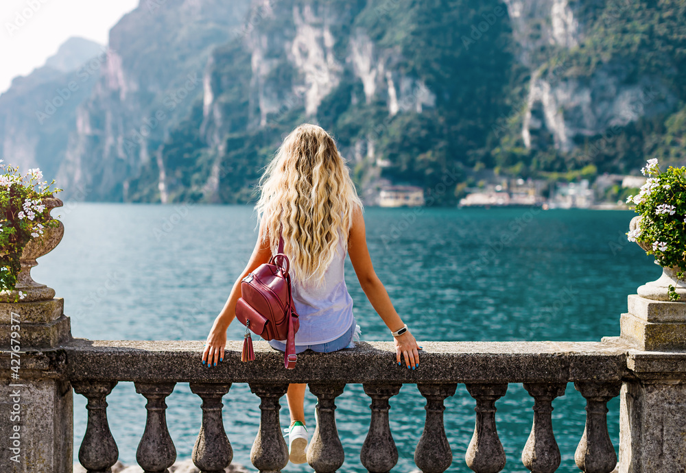 Young girl looks on the mountain and blue water of the Garda lake. Back view, vacation concept