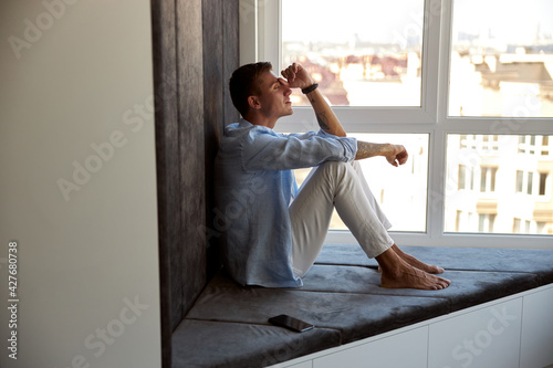Wallpaper Mural Happy adult caucasian male is sitting near panoramic window and chilling Torontodigital.ca