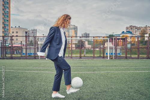 girl in an office suit hitting hitting soccer ball on the stadium field. concept photo