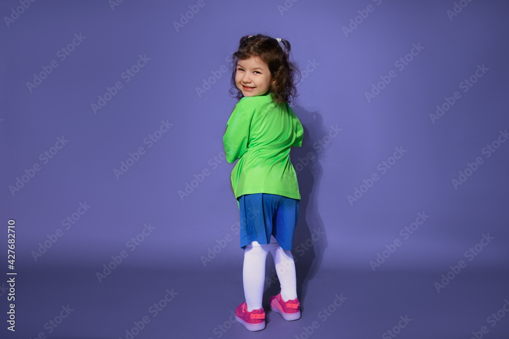 Φωτογραφία Funny little girl in football uniform stands with her back on purple background