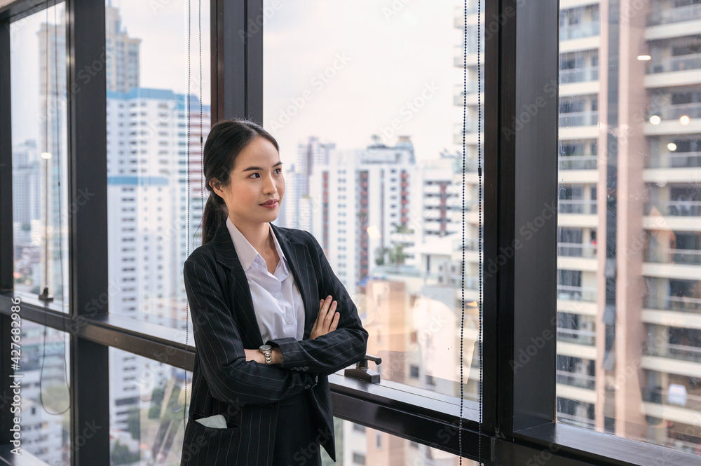 Young asian businesswoman standing crossed arms by window in the office Young asian businesswoman standing crossed arms by window in the office