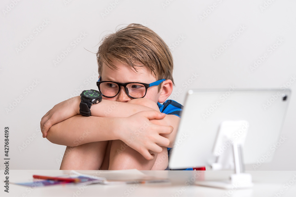 Stressed kid. Coronavirus outbreak. Lockdown and school closures. School boy watching online education classes feeling bored and depressed at home. COVID-19 pandemic forces children online learning. Stressed kid. Coronavirus outbreak. Lockdown and school closures. School boy watching online education classes feeling bored and depressed at home. COVID-19 pandemic forces children online learning.
