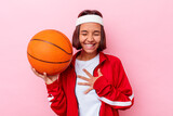 Young mixed race woman playing basketball isolated on pink background laughs out loudly keeping hand on chest.