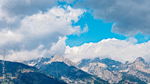 Tall Rocky Mountains in blue sky with white clouds. © John