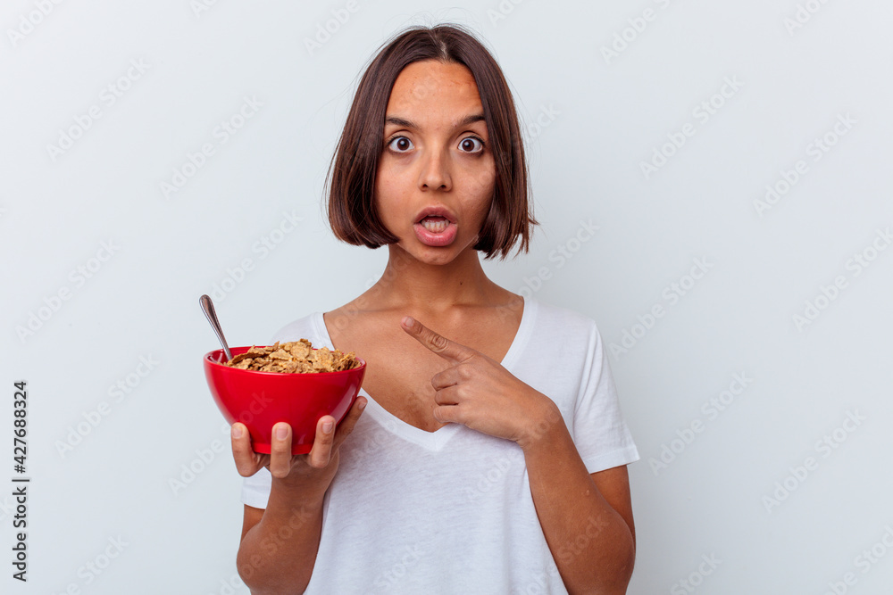 Young mixed race woman eating cereals isolated on white background pointing to the side Young mixed race woman eating cereals isolated on white background pointing to the side