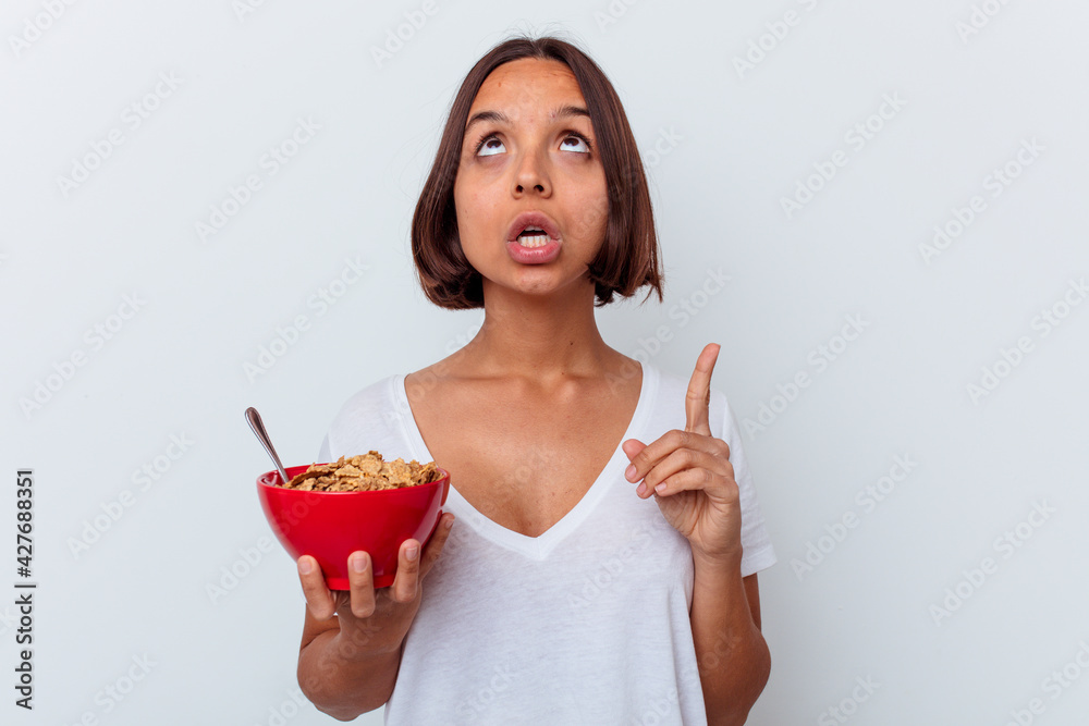 Young mixed race woman eating cereals isolated on white background pointing upside with opened mouth. Young mixed race woman eating cereals isolated on white background pointing upside with opened mouth.