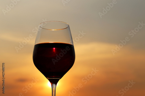 Glass with red wine on sunset background, evening sun is shining through the glass. Concept of celebration, wine industry