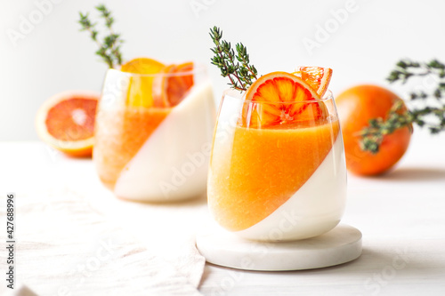Panna cotta orange desserts decorated with oranges and thyme stand on white background, close-up, horizontal orientation, selective focus on thyme photo