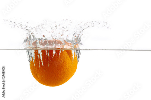 one ripe juicy orange falls into the water with splashes on a white background
