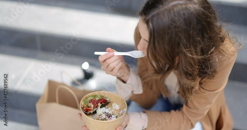Young businesswoman eating healthy takeaway food with tuna and rise, while sitting on the stairs outdoors