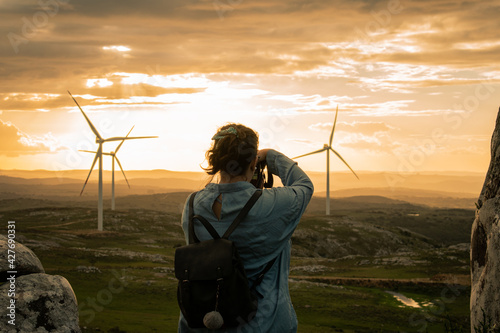 Woman taking photos at sunset over the mountain range with windmills