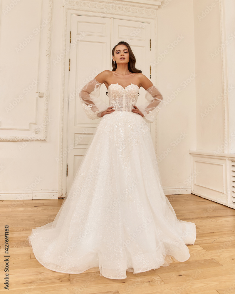 Elegant caucasian woman with natural make-up and hairstyle wearing white bridel dress, standing and posing in bright stylish interior. Full length portrait Elegant caucasian woman with natural make-up and hairstyle wearing white bridel dress, standing and posing in bright stylish interior. Full length portrait