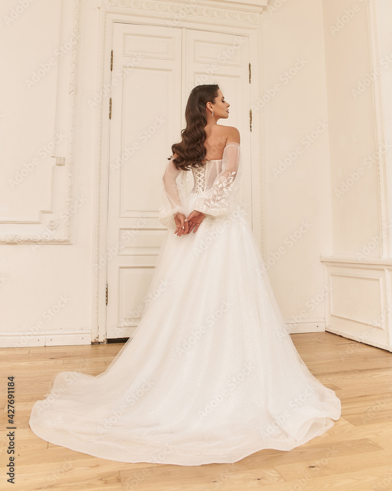 Elegant caucasian woman with natural make-up and hairstyle wearing white bridel dress, standing and posing in bright stylish interior. Full length portrait Elegant caucasian woman with natural make-up and hairstyle wearing white bridel dress, standing and posing in bright stylish interior. Full length portrait
