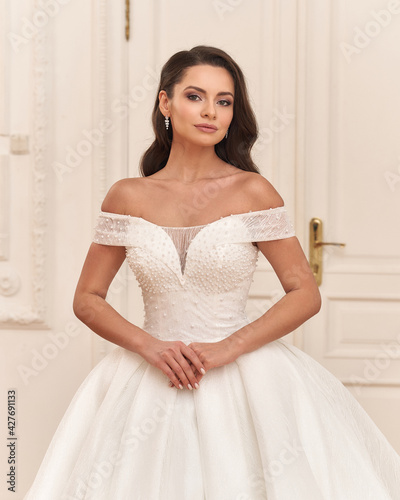 Elegant caucasian woman in white bridal dress standing and posing in bright interior