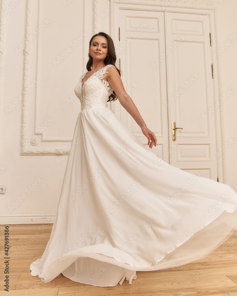 Young pretty caucasian woman standing in bright empty interior and posing in elegant wedding dress Young pretty caucasian woman standing in bright empty interior and posing in elegant wedding dress