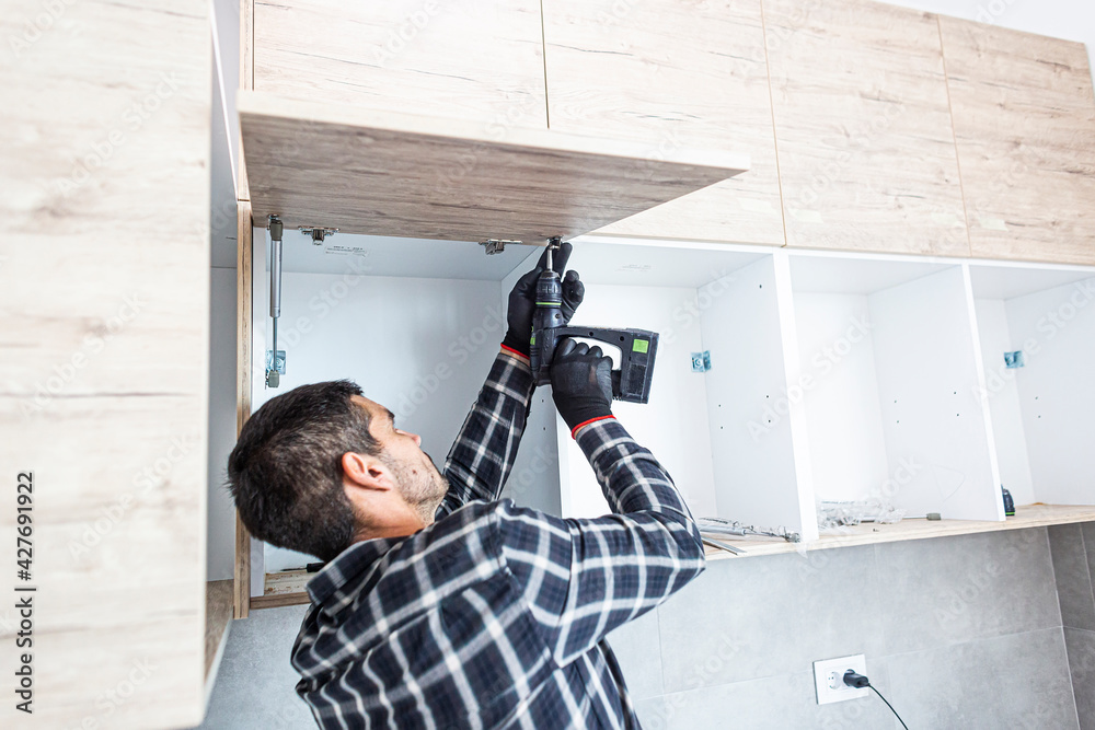 The carpenter sets the door of the kitchen shelves