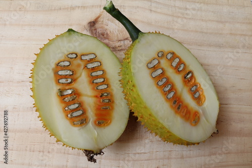 Gac fruit (Momordica cochinchinensis), green fresh fruits and vegetables two halves slice isolated on wooden flooring background closeup. photo