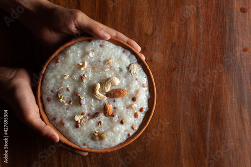 Close-up of Creamy Sabudana Kheer Garnished with dry fruits. Indian delicious dessert. Served in earth sole pot hold by hand. Top View on wooden background. photo