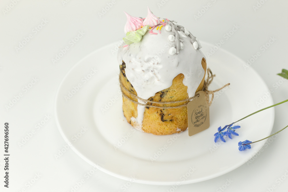 Orthodox Easter cake tied with a rope with a tag on a plate with spring flowers in a pot side view on a white background Orthodox Easter cake tied with a rope with a tag on a plate with spring flowers in a pot side view on a white background