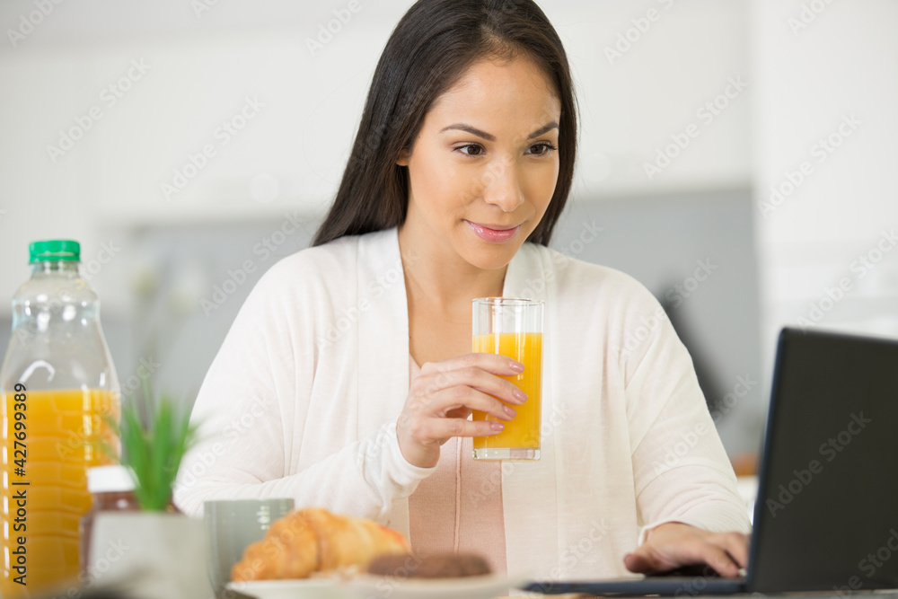 positive woman with juice using laptop in the kitchen positive woman with juice using laptop in the kitchen