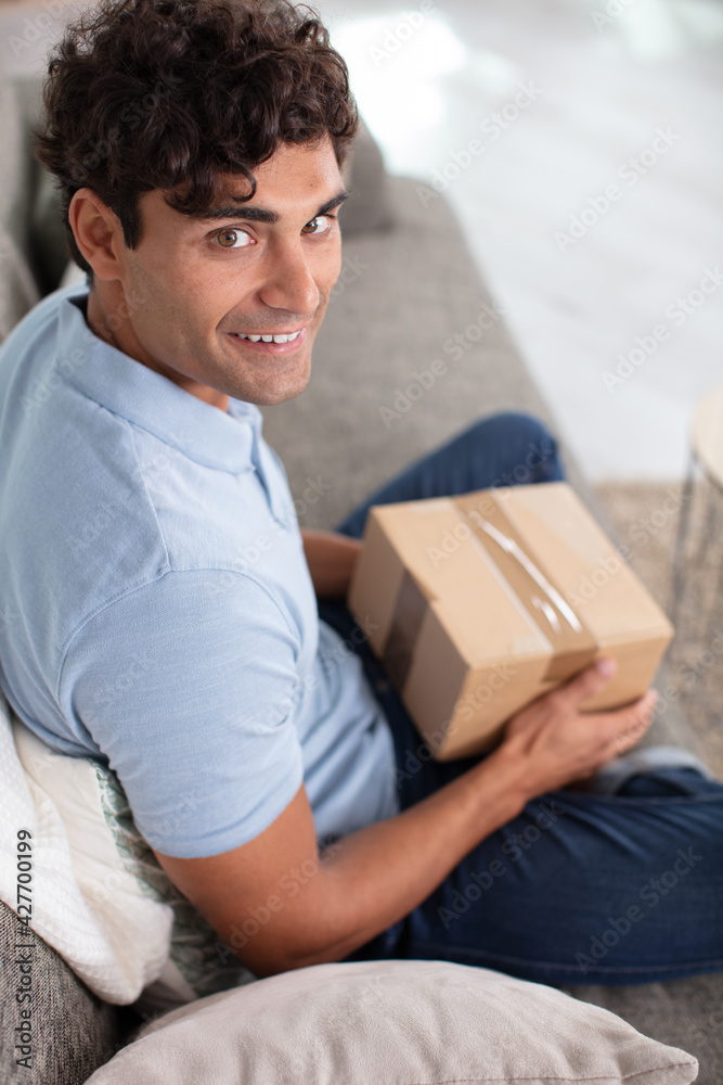 handsome young man opening parcel while sitting on sofa handsome young man opening parcel while sitting on sofa
