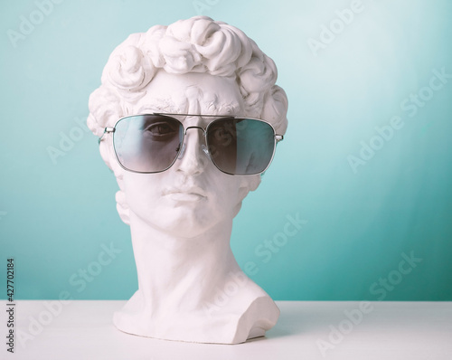 Plaster statue head blue background wearing sunglasses