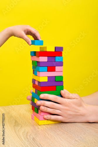 Hands close up playing a round of family game removing blocks from the tower with wooden blocks. Planning, risk, and strategy in business or building.