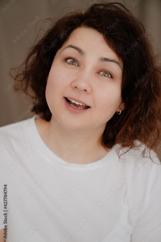 Portrait of a smiling brunette woman with curly hair in a white T-shirt. Portrait of a smiling brunette woman with curly hair in a white T-shirt.