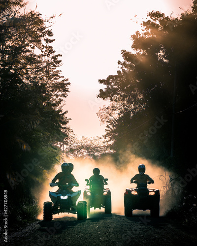 Silhouette of friends driving quad bike at sunset