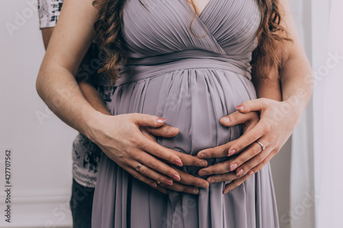 Pregnant girl in a dress holds her hands on her belly 