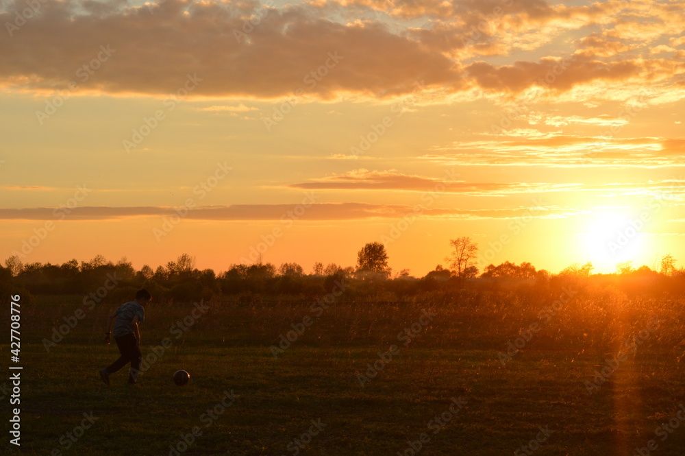 silhouette of a boy playing with a ball at sunset