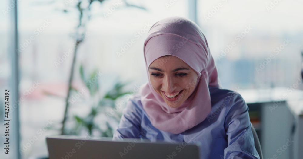 Attractive young arabic woman using laptop computer in the corporate office. Smiling successful Muslim office manager female at workspace. Attractive young arabic woman using laptop computer in the corporate office. Smiling successful Muslim office manager female at workspace.